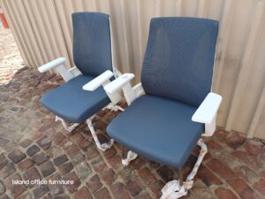 Two Moritz Ergonomic Visitors chairs in grey with white armrests, displayed on a cobblestone surface.